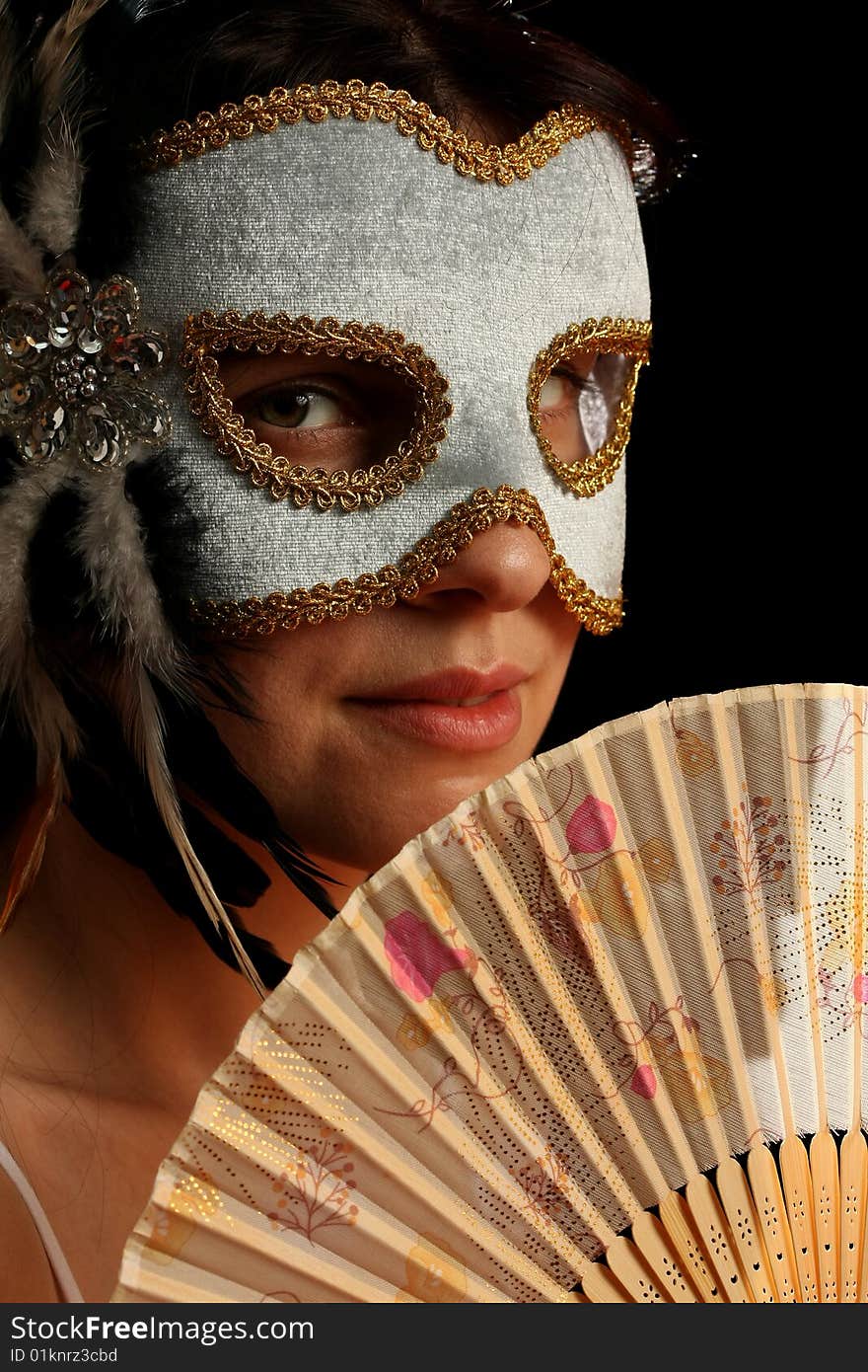 Young brunette with venetian mask and spanish fan, on black