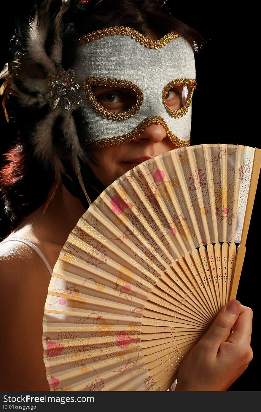 Young brunette with venetian mask and spanish fan, on black