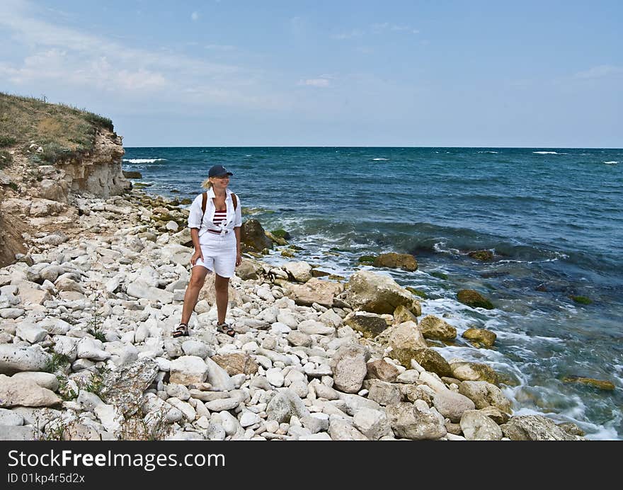 A happy smiling woman is standing on the rocky seashore looking at sea. A happy smiling woman is standing on the rocky seashore looking at sea