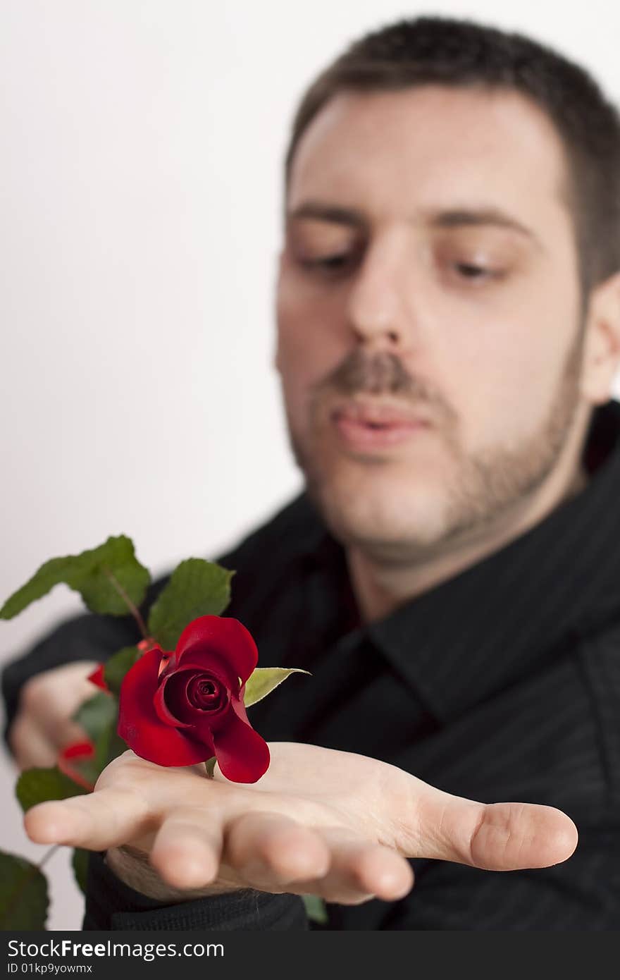 Young man, holding a beautiful red rose on his open palm, blowing in its direction. Young man, holding a beautiful red rose on his open palm, blowing in its direction