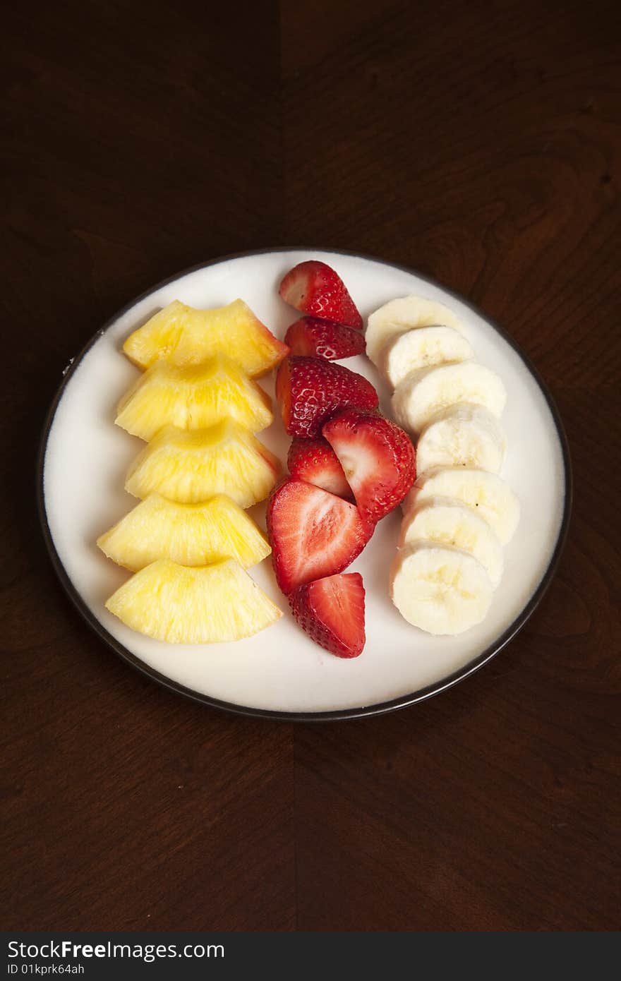 A plate of fresh fruit slices on a table with strawberry, pineapple, and banana