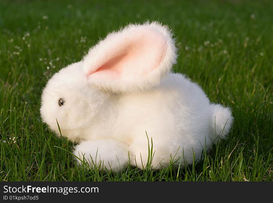 A toy white hare is on green grass