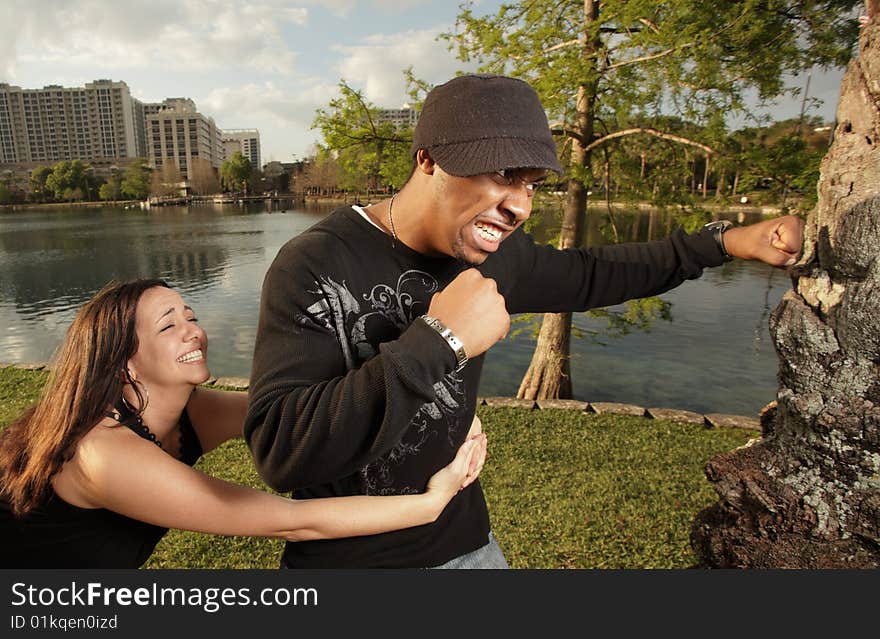 Man fighting a tree while his girlfriend is trying to hold him back