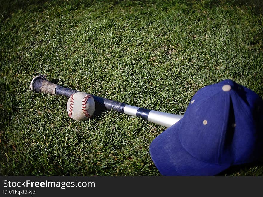 A baseball and a bat and hat on a grassy baseball field. Tilt shift lens used. A baseball and a bat and hat on a grassy baseball field. Tilt shift lens used