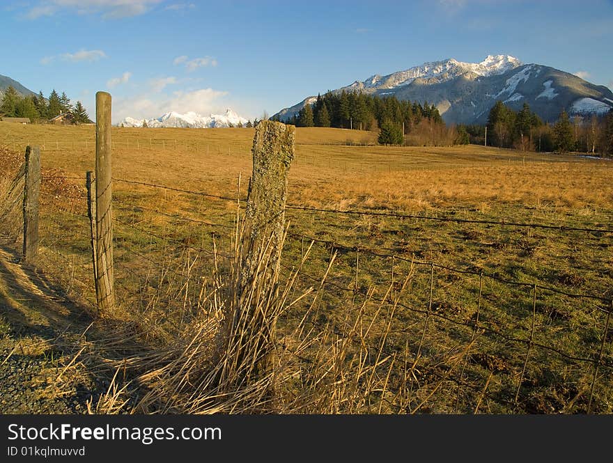 A scenic view of snow covered mountains from a fenced rural pasture