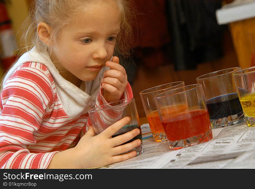 A young girl examins one of the many glasses at her table with colorful liquid in them. A young girl examins one of the many glasses at her table with colorful liquid in them.