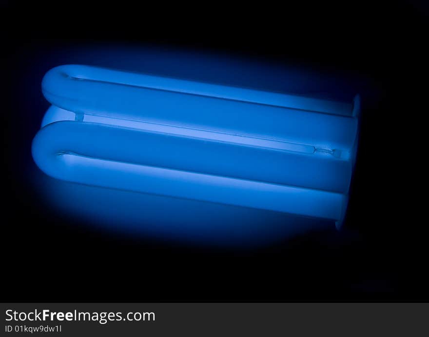 Energy saving lamp (light bulb) with dark blue colour on the black background. Energy saving lamp (light bulb) with dark blue colour on the black background