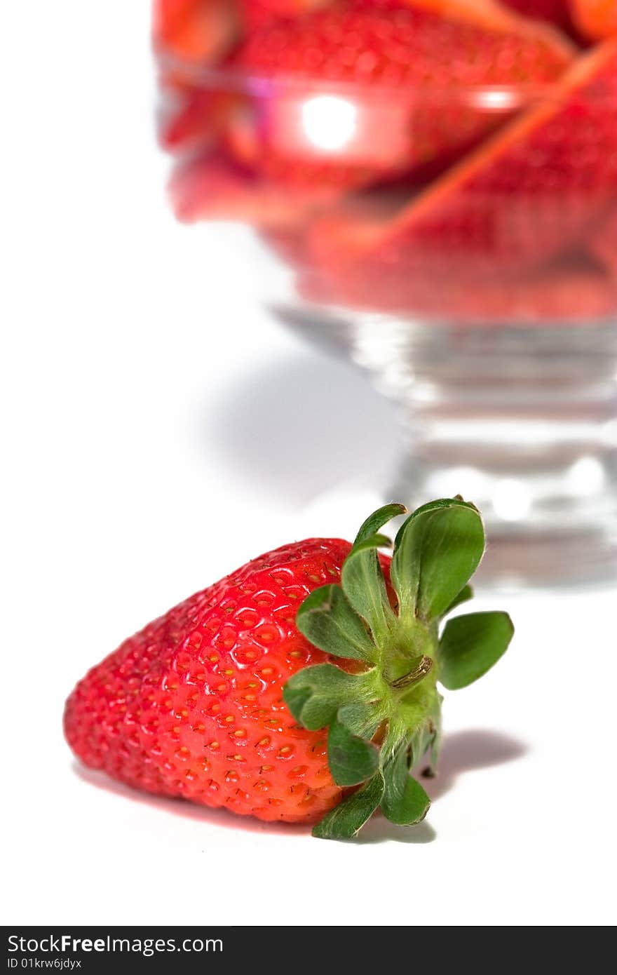 Isolated strawberry in front of bowl of cut strawberries. Isolated strawberry in front of bowl of cut strawberries.