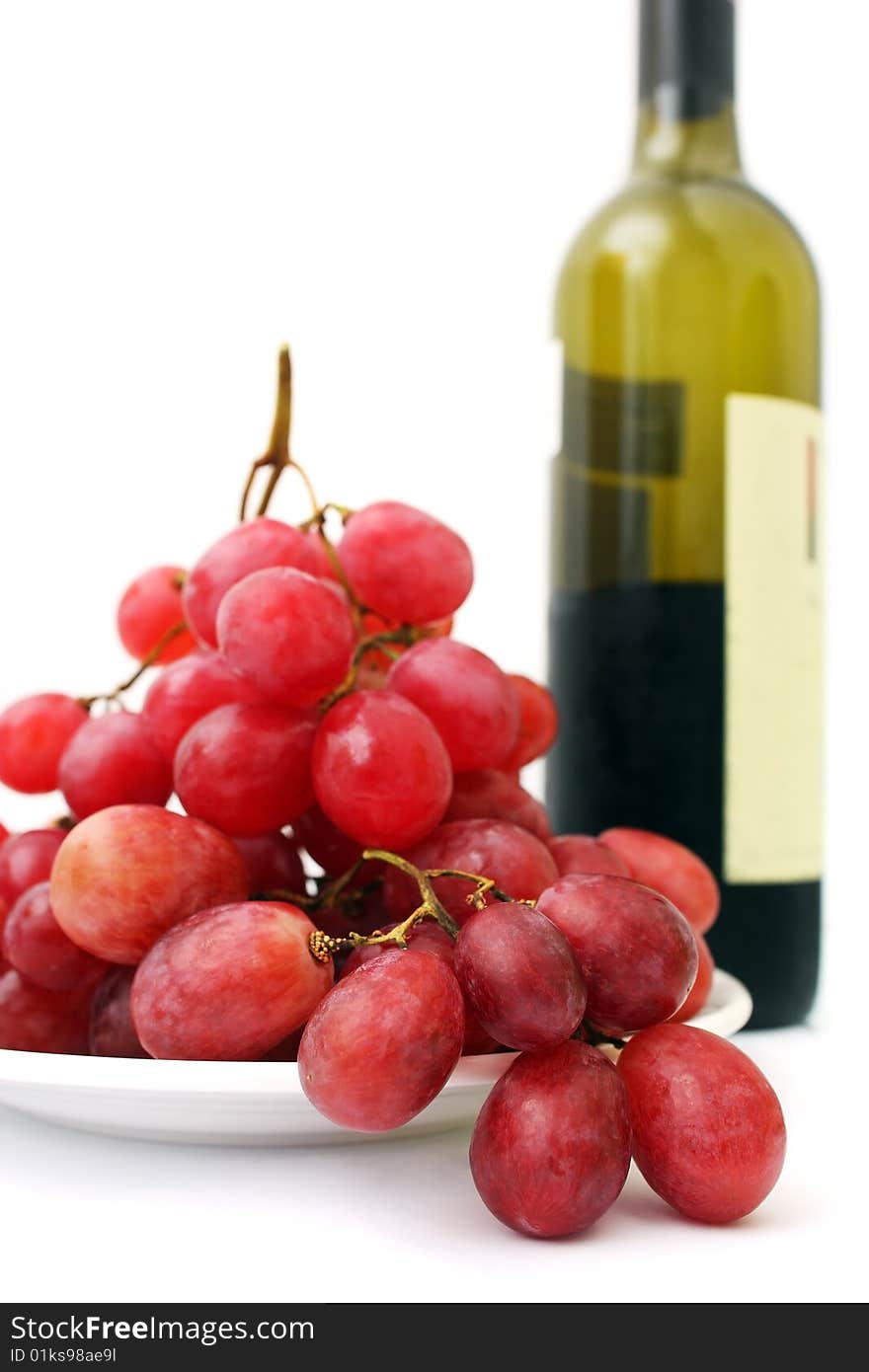 Bunch of red grapes on white plate beside wine bottle. Bunch of red grapes on white plate beside wine bottle.