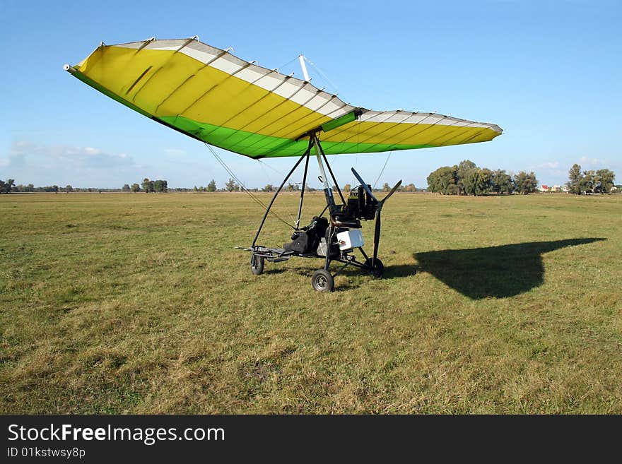 Yellow and green microlight on the field and its shadow on grass. Yellow and green microlight on the field and its shadow on grass