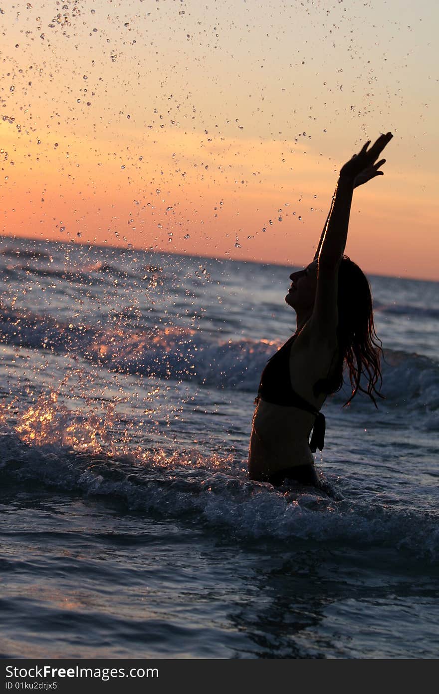 Woman splashing by sunset in the caribbean ocean