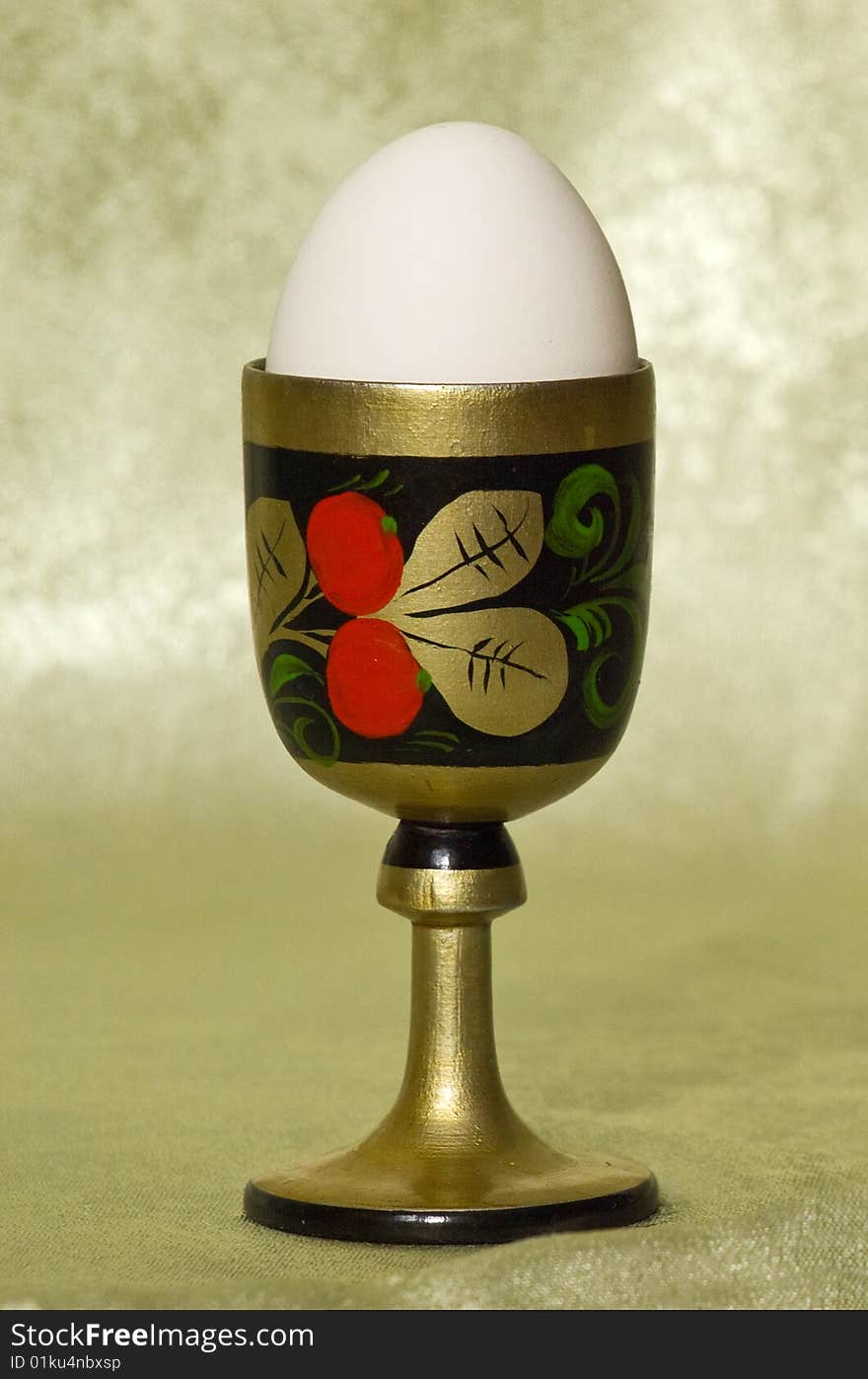 White egg in a wooden stand with a picture on a green background