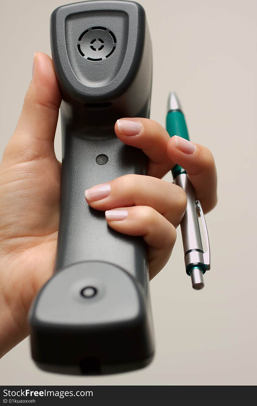 Female hand holding a business telephone handset with her left hand, also holding a pen to take notes. Female hand holding a business telephone handset with her left hand, also holding a pen to take notes