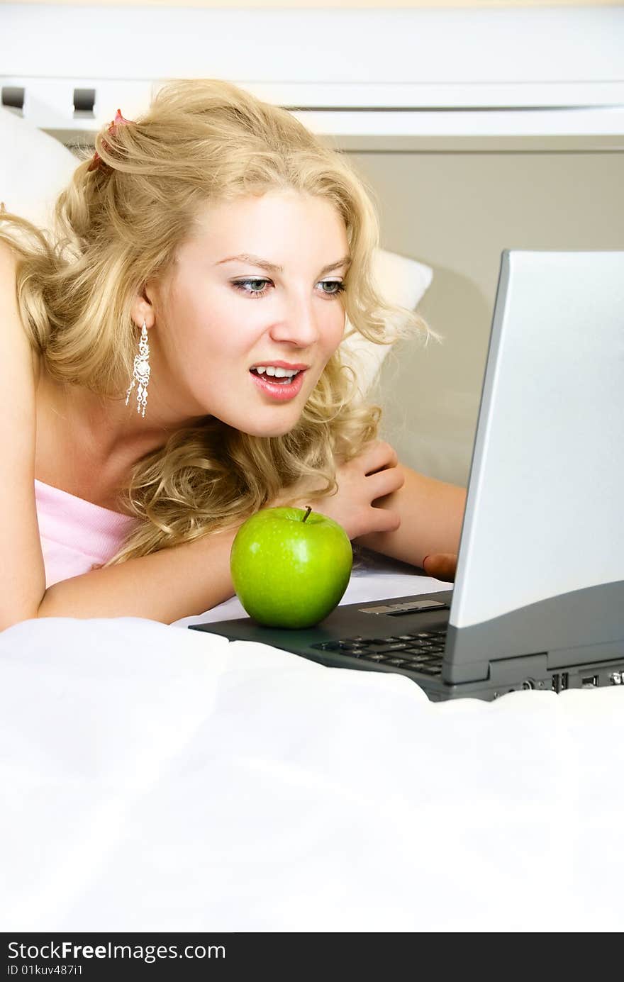 Beautiful girl at home on the bed using a laptop and eating a green apple. Beautiful girl at home on the bed using a laptop and eating a green apple