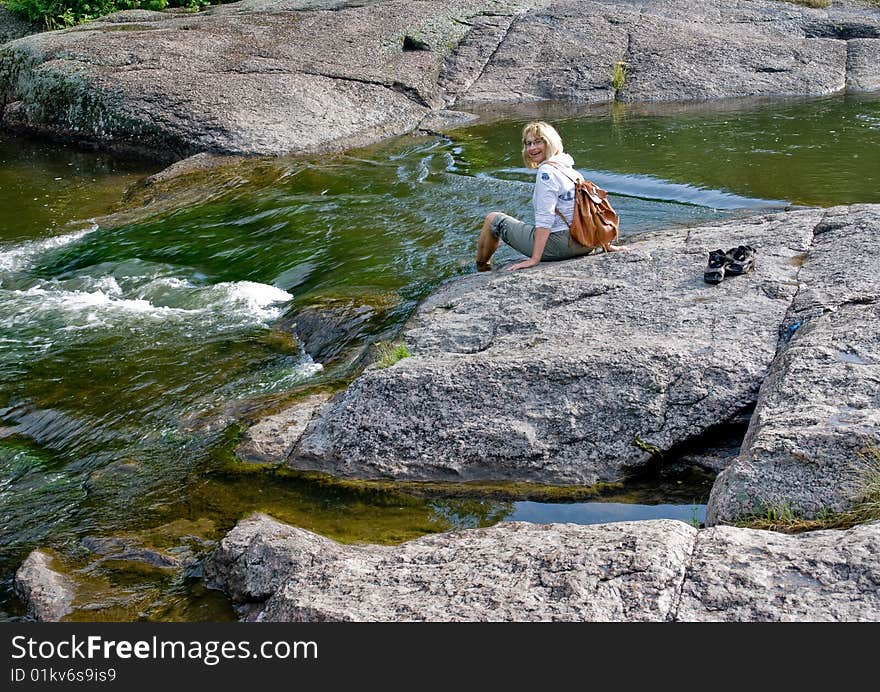 A happy woman on big stone beside rapid stream.