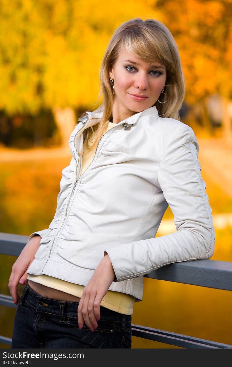 Pretty girl in white jacket near fence with blurry yellow autumn background