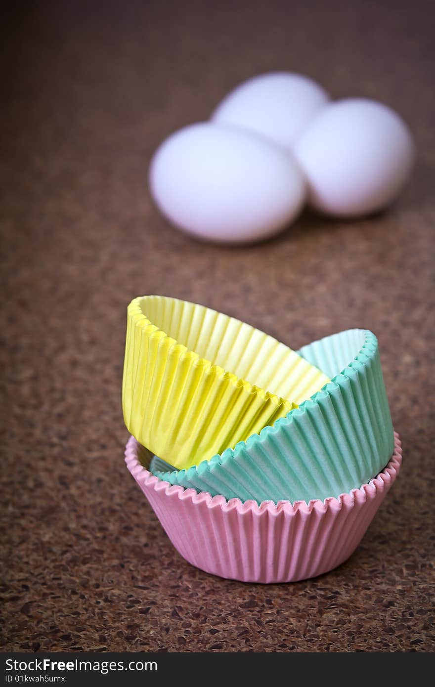 Pastel colored cupcake holders in foreground with three eggs out of focus in background