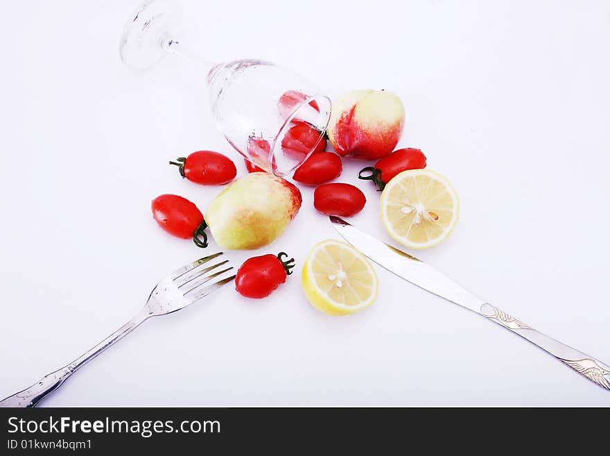 Peachs , peper , lemon and tomatoes on white background with goblet, water in it, knife and fork on desk. Peachs , peper , lemon and tomatoes on white background with goblet, water in it, knife and fork on desk