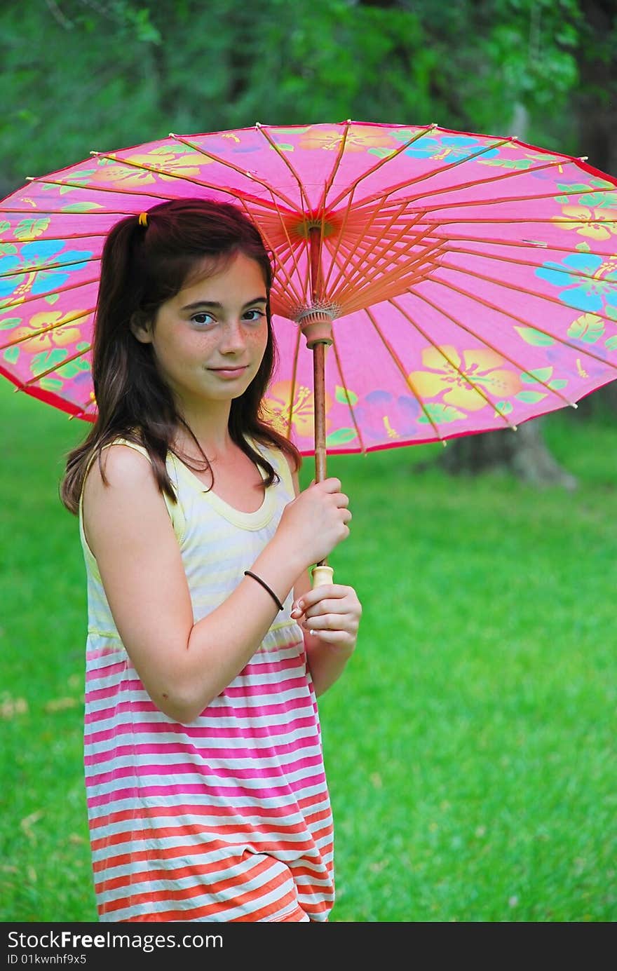 Beautiful 10 year old brown haired girl holding a parasol outdoors in the park. Beautiful 10 year old brown haired girl holding a parasol outdoors in the park