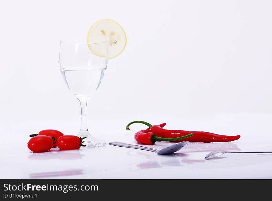 Peper and tomatoes, lemon on white background with goblet, water in it, spoon on desk. Peper and tomatoes, lemon on white background with goblet, water in it, spoon on desk