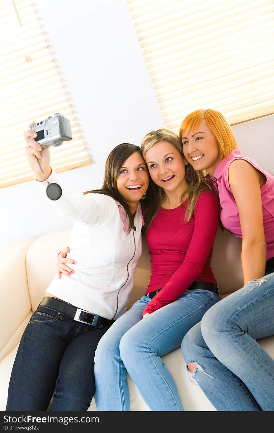 Three happy girls sitting on couch. One of them taking a picture. Three happy girls sitting on couch. One of them taking a picture.