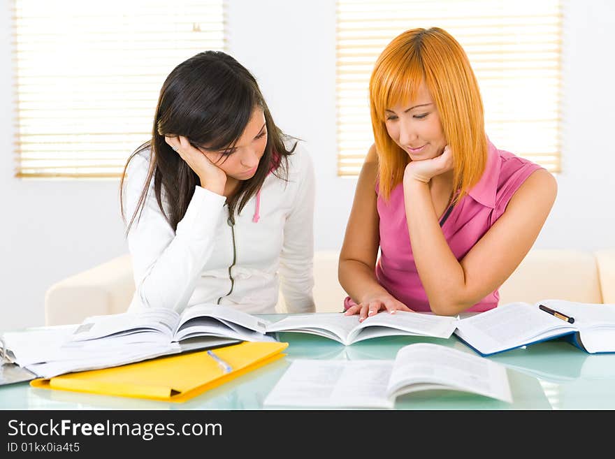 Two girls sitting at the table and doing homework.They're reading book and taking notes. Front view. Two girls sitting at the table and doing homework.They're reading book and taking notes. Front view.