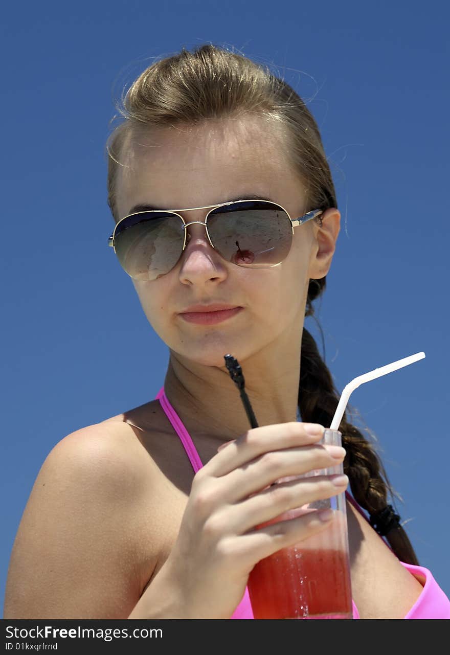 The young woman with juice on a beach against the blue sky. The young woman with juice on a beach against the blue sky