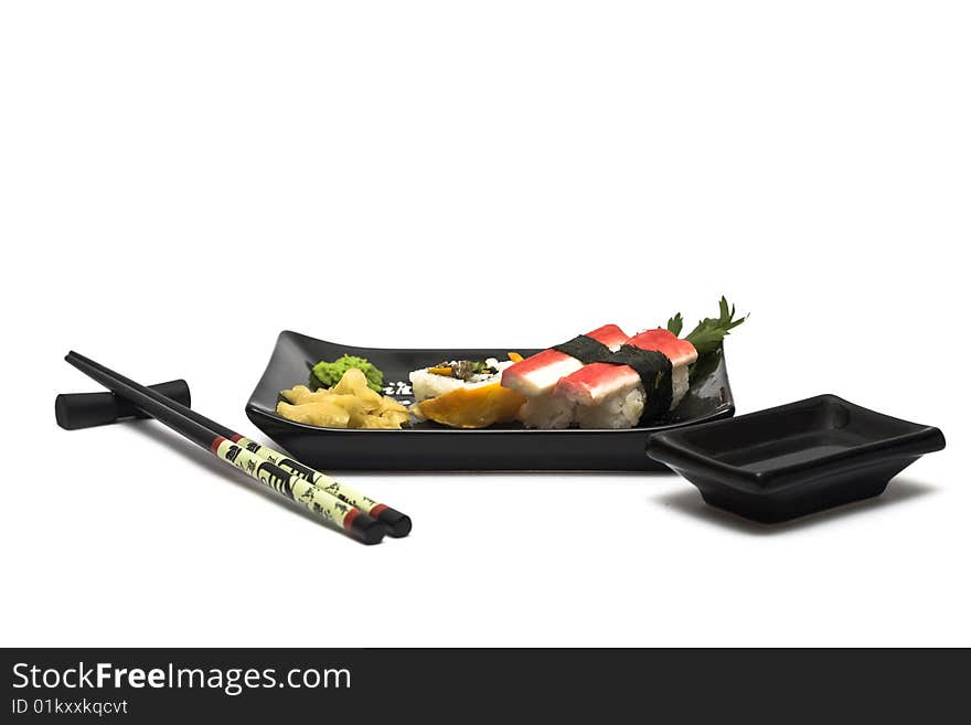 A set of sushi on a black plate with wasabi and gari, isolated on a white background, wish hashi ans soy sauce. A set of sushi on a black plate with wasabi and gari, isolated on a white background, wish hashi ans soy sauce.