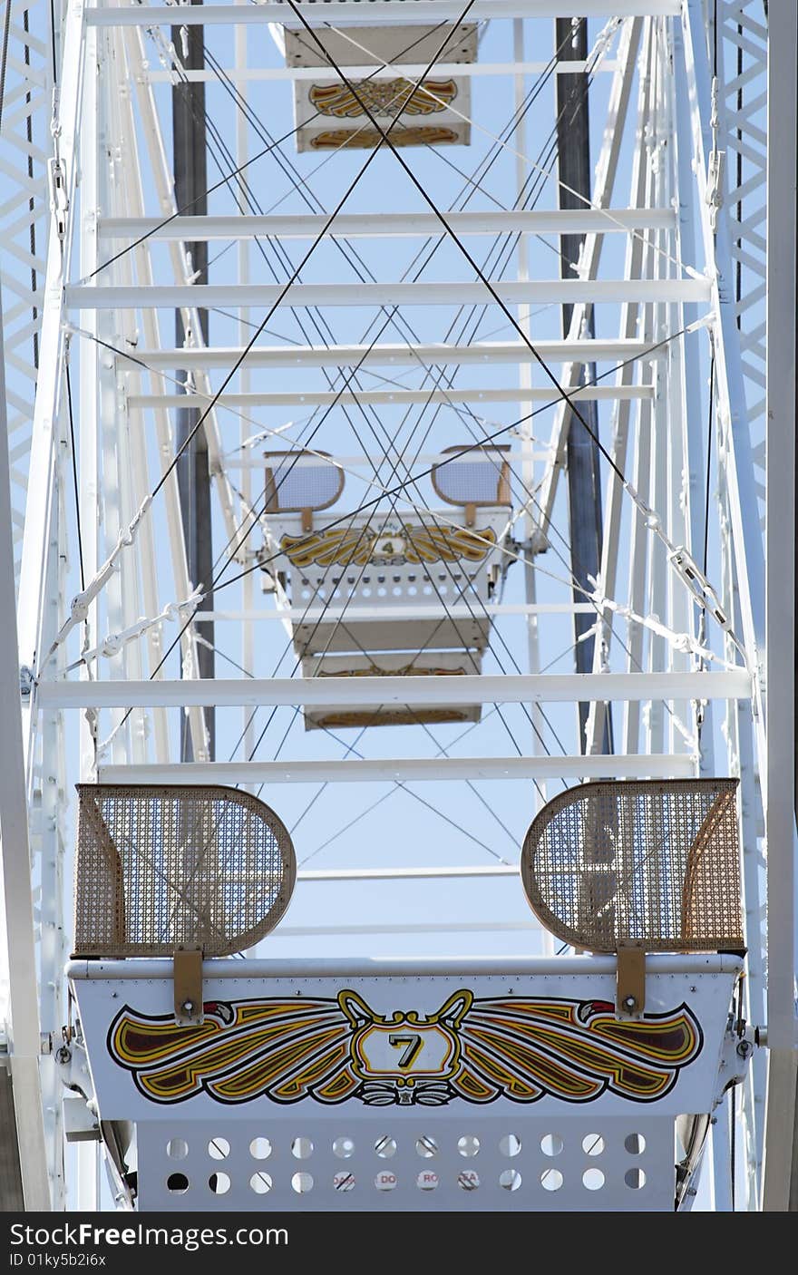 Empty ferris wheel seats with a blue sky.