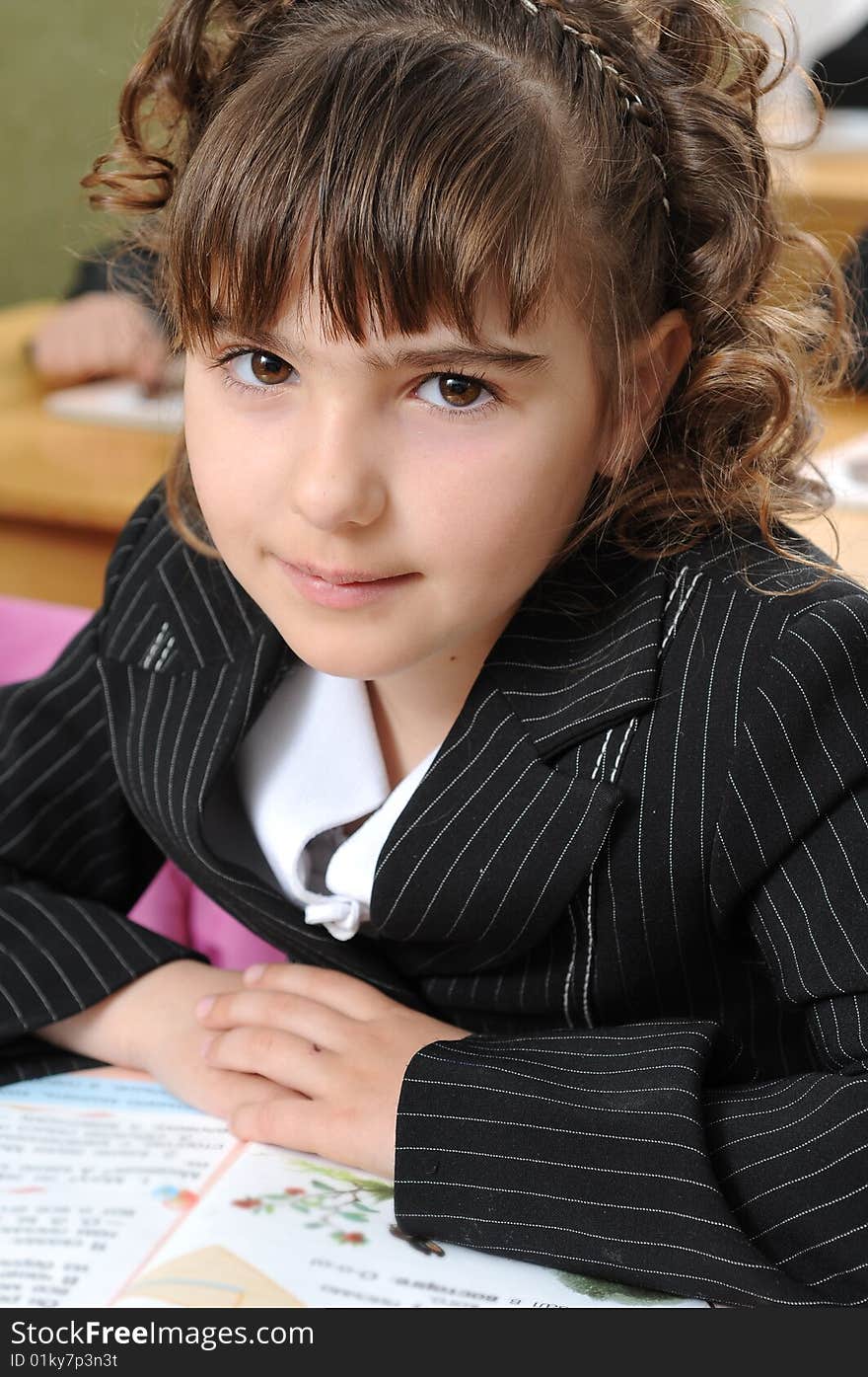 The girl the first-grader sits at school at a lesson and modestly smiles. The girl the first-grader sits at school at a lesson and modestly smiles.