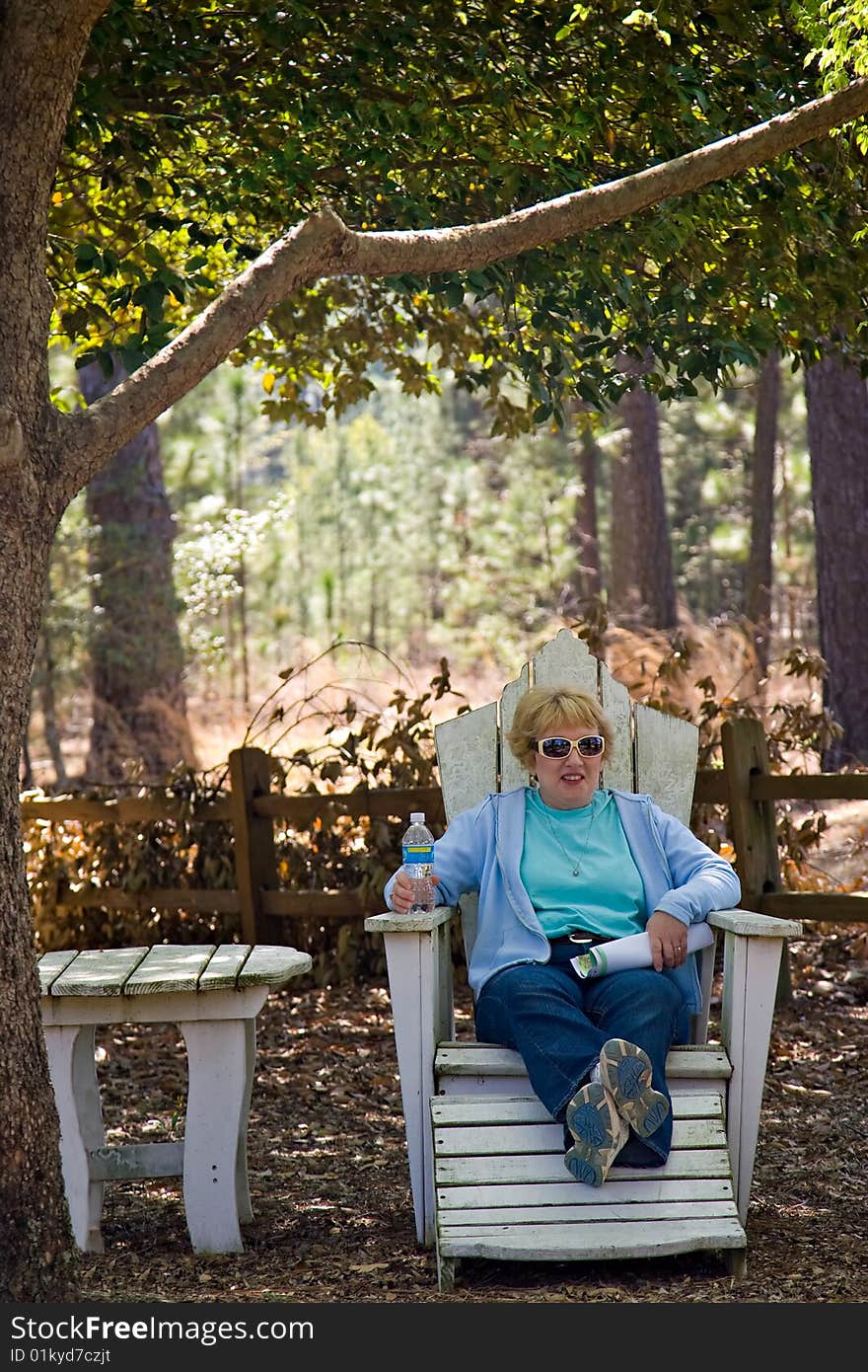 Woman resting under tree on white painted outdoor furniture. Woman resting under tree on white painted outdoor furniture