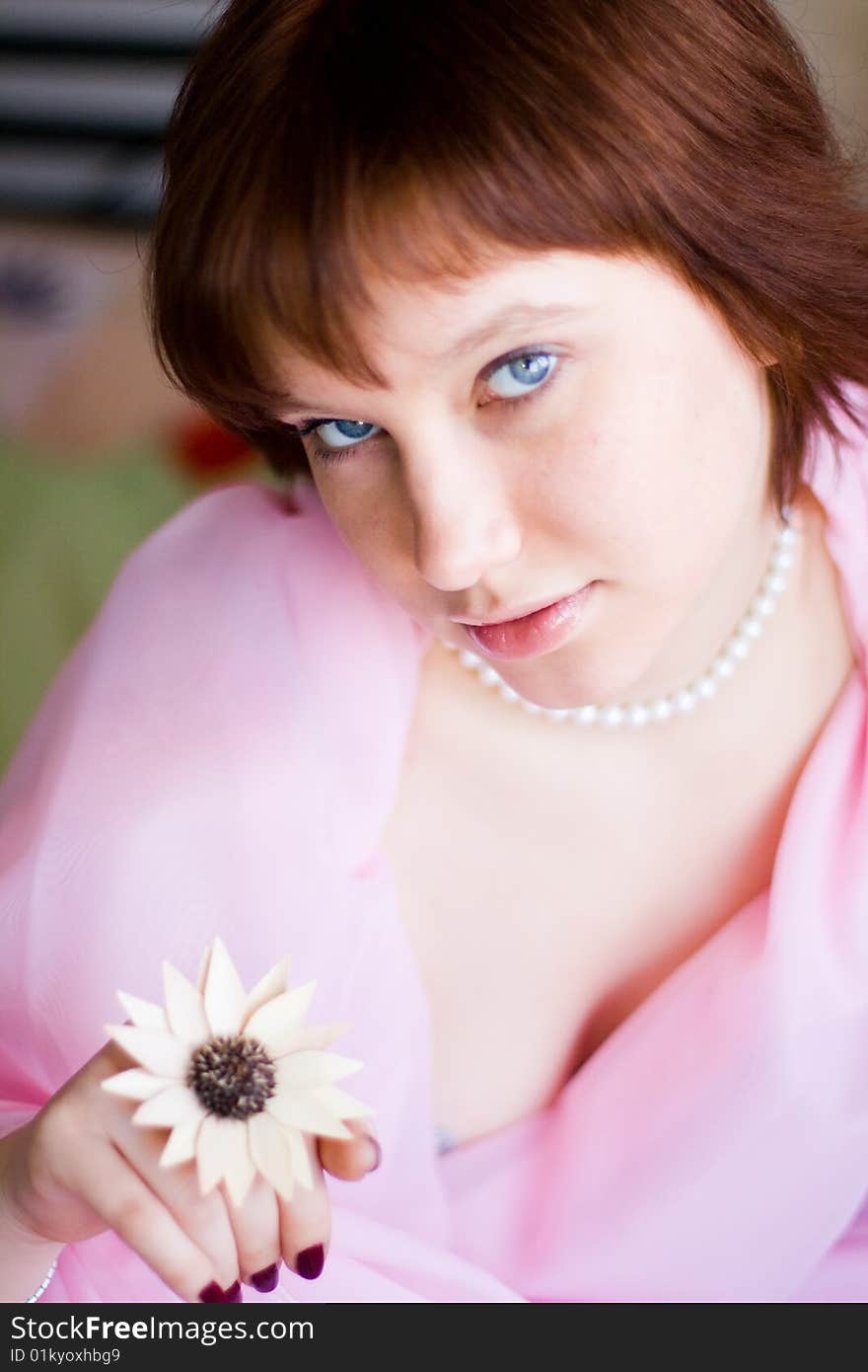 The girl looks expressive blue eyes, a pink dress, holds a flower in her hand. The girl looks expressive blue eyes, a pink dress, holds a flower in her hand