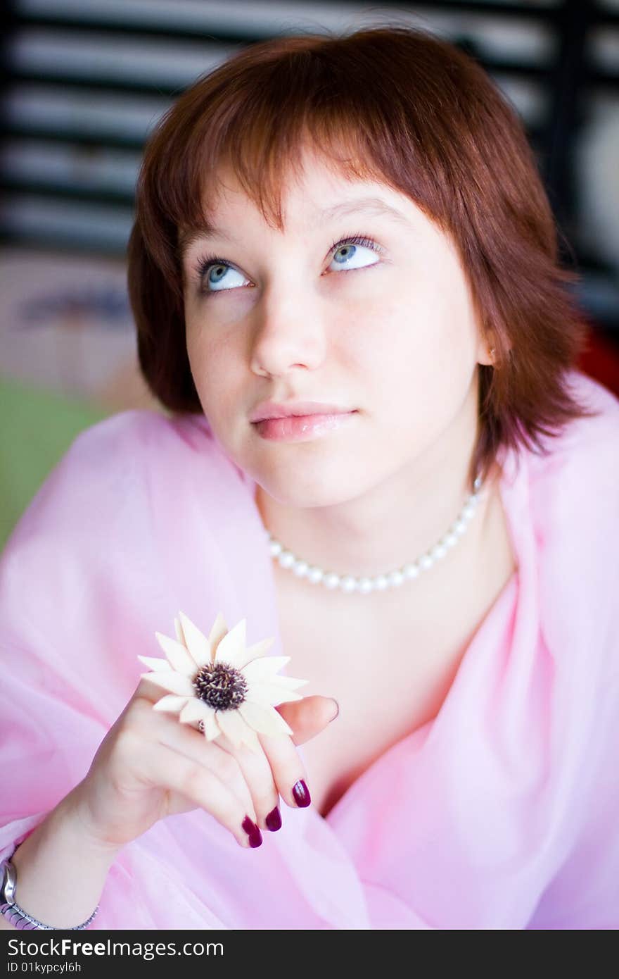 The girl looks expressive blue eyes, a pink dress, holds a flower in her hand. The girl looks expressive blue eyes, a pink dress, holds a flower in her hand