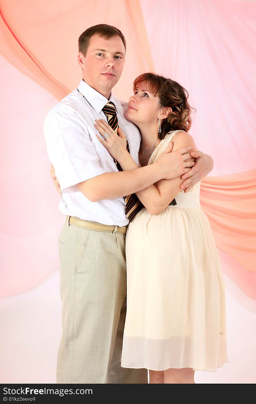 Young beautiful married couple the birth of the first child wait. Pink background. New photos every week