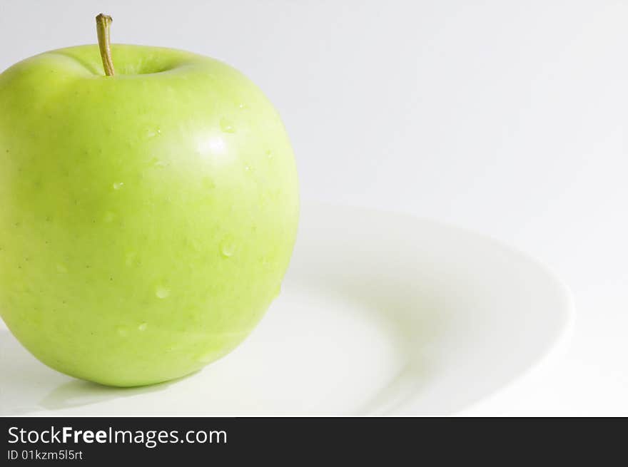 Single fresh, green apple, slightly cropped, on dish with white background. Horizontal image with copy-space. Single fresh, green apple, slightly cropped, on dish with white background. Horizontal image with copy-space