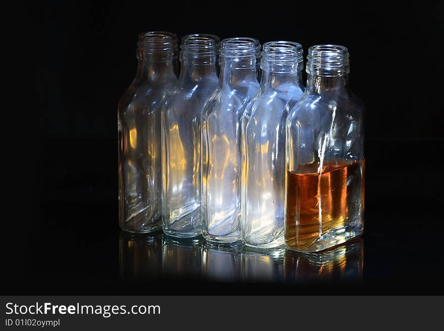 Four empty and one bottle with cognac on dark background. Four empty and one bottle with cognac on dark background