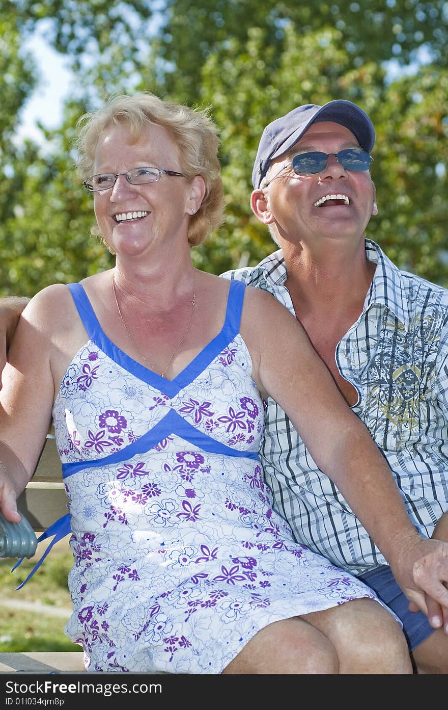 Aged couple sitting on a bench and laughing out loud