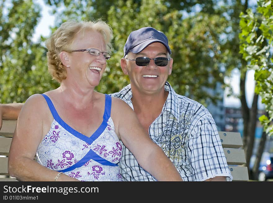 Aged couple sitting on a bench and laughing out loud