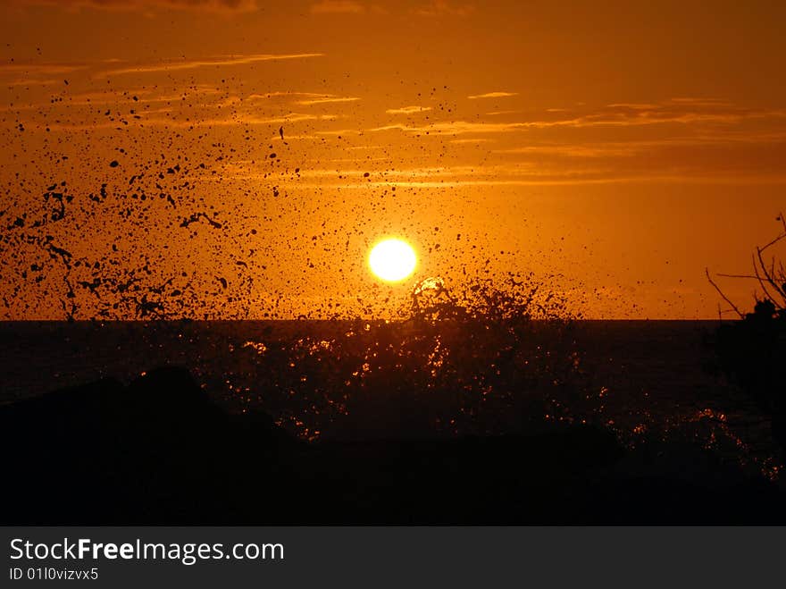 A beautiful, orange sunset with waves crashing in the foreground.