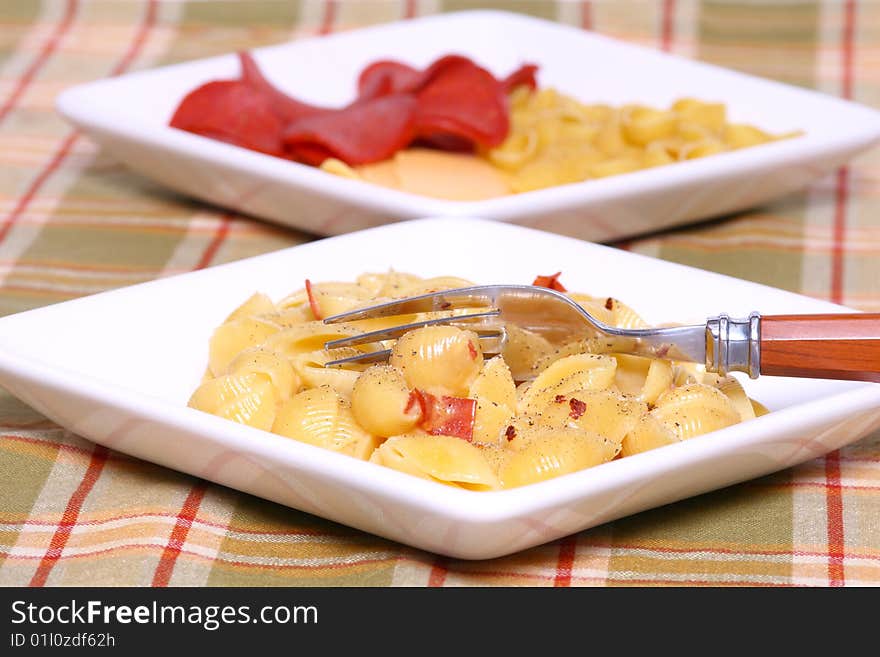 Macaroni and pepperoni on a white plate with ingredients in the background with fork