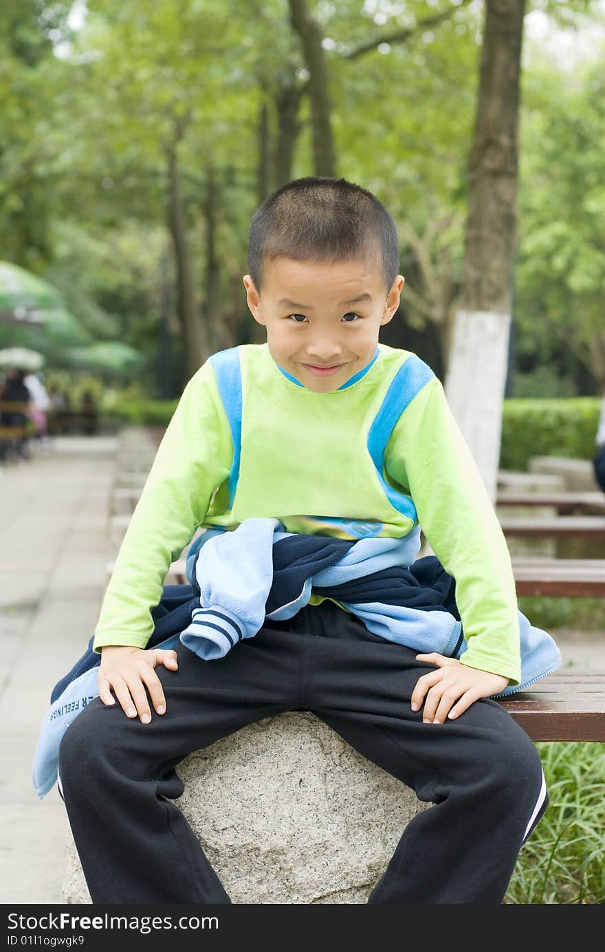 A Chinese kid sit beside a tree. A Chinese kid sit beside a tree