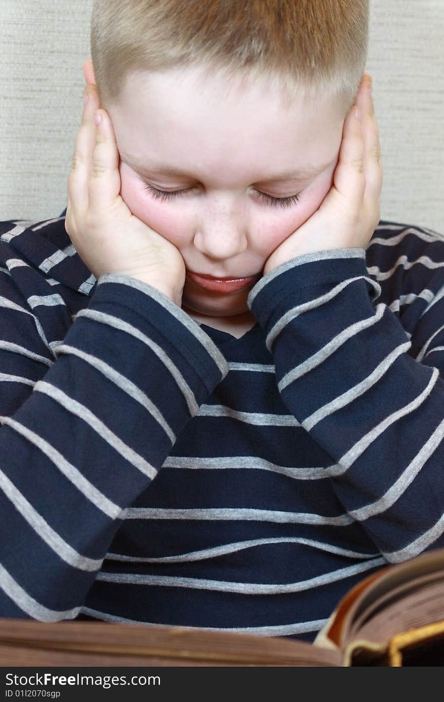 A boy is sitting with closed eyes holding his head. A boy is sitting with closed eyes holding his head