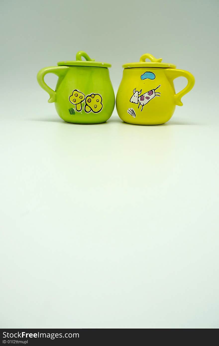 A green cup and a yellow cup with cute cartoon decoration. A green cup and a yellow cup with cute cartoon decoration.