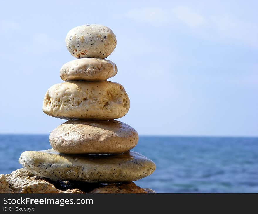 The pyramid of stones on a background of sea and sky with the horizon line in the sun clear cloudless day. The pyramid of stones on a background of sea and sky with the horizon line in the sun clear cloudless day