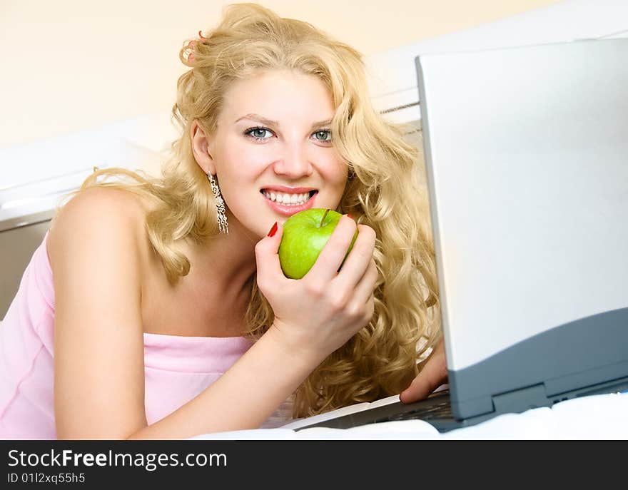 Beautiful girl at home on the bed using a laptop and eating a green apple. Beautiful girl at home on the bed using a laptop and eating a green apple