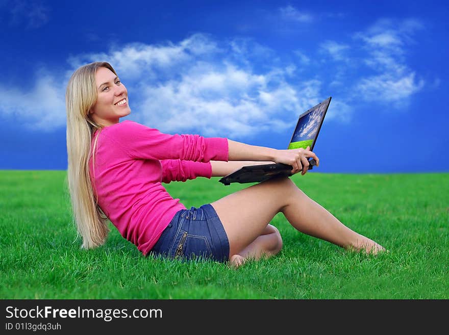 Beautiful girl with laptop on the blue sky and green grass background. Beautiful girl with laptop on the blue sky and green grass background