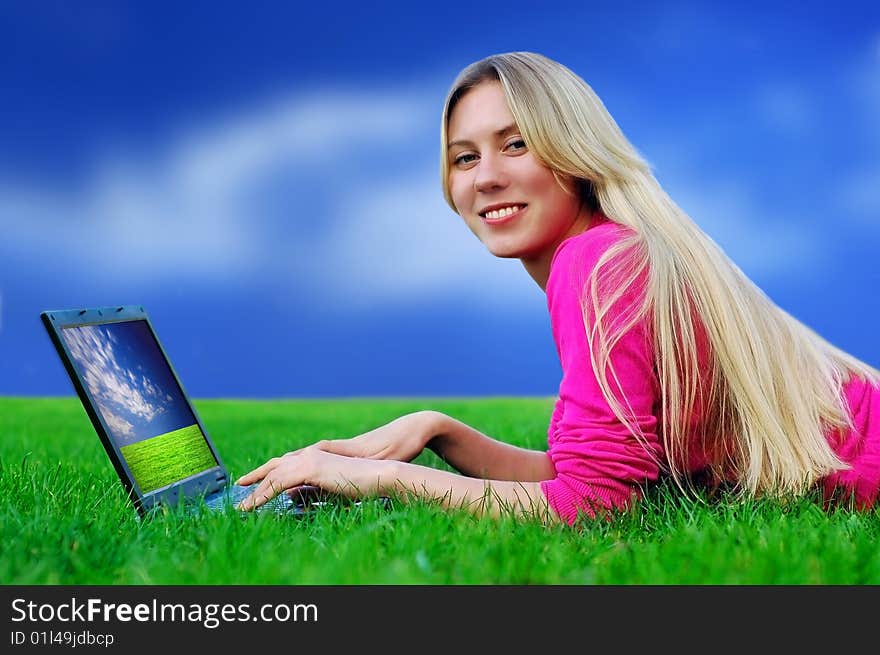 Beautiful girl with laptop on the blue sky and green grass background. Beautiful girl with laptop on the blue sky and green grass background