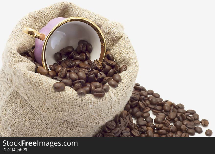 The cup lies in a sack with coffee grains is isolated on white