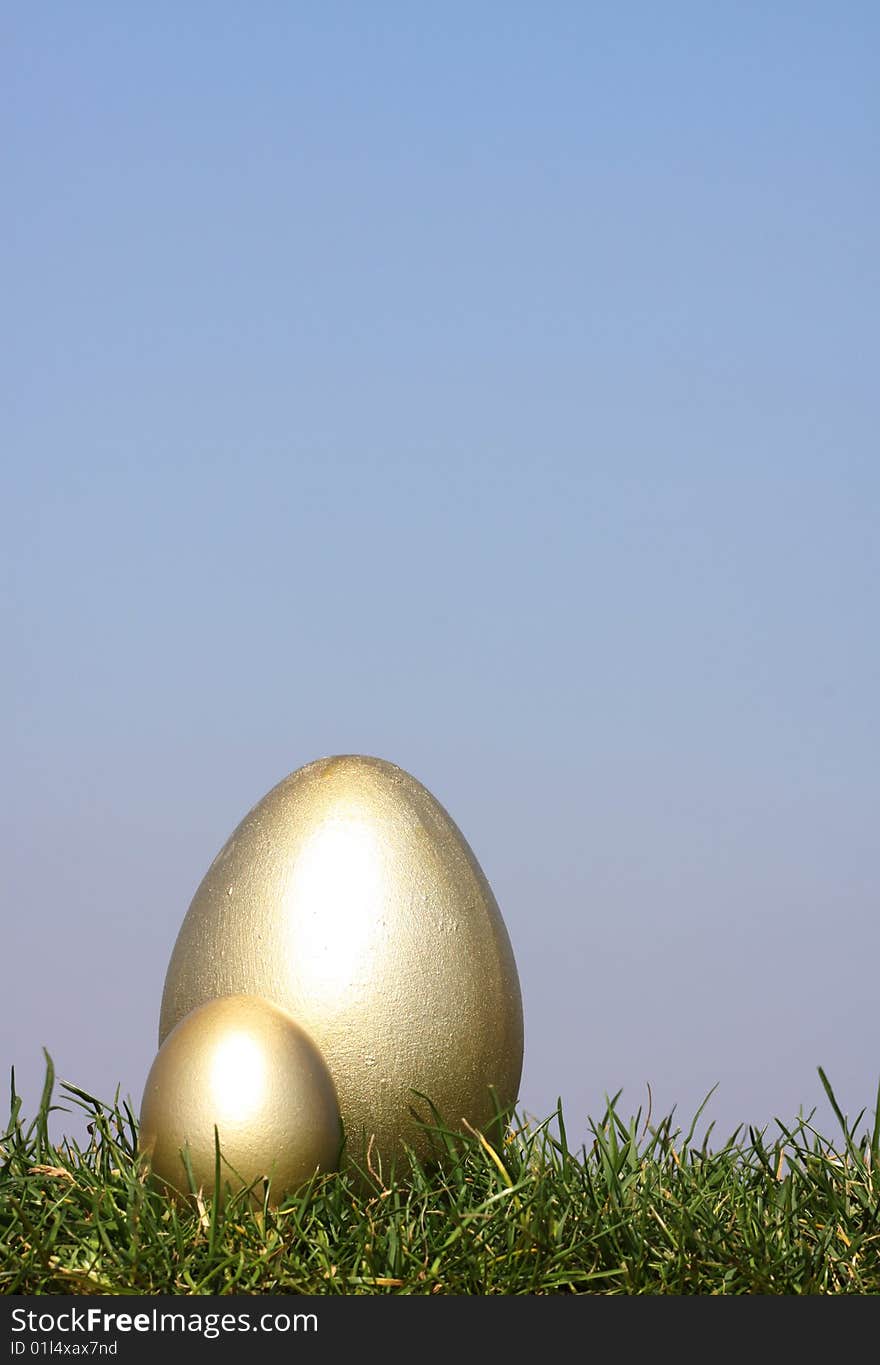 2 Gold Easter eggs in grass against  a bright blue sky