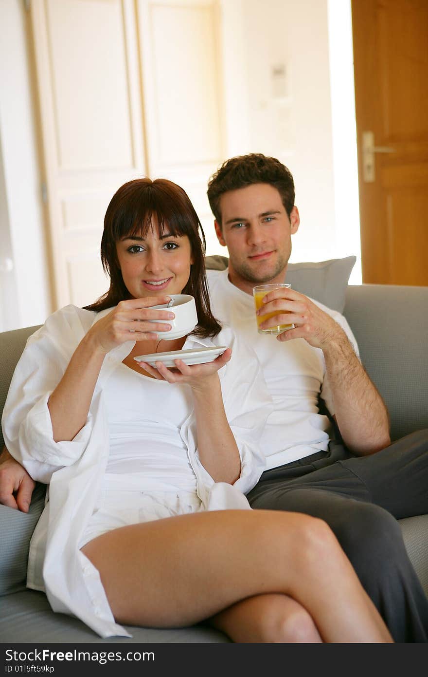 Young man and young woman sitting on a sofa, drinking coffee and orange juice. Young man and young woman sitting on a sofa, drinking coffee and orange juice